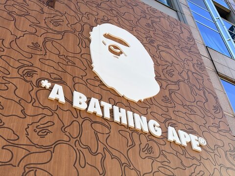 A Bathing Ape (BAPE) flagship store exterior signage featuring the iconic white Ape Head logo and brand name on a wood camouflage pattern wall - Osaka, Japan, December 25, 2025