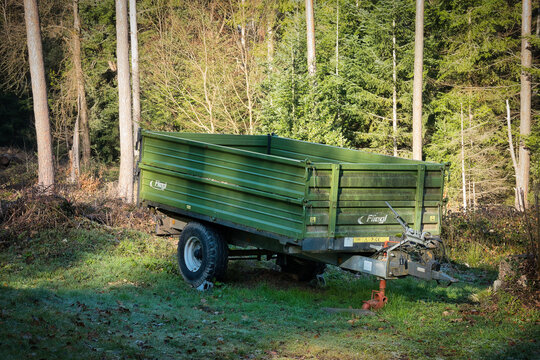 Ein gr&uuml;ner, einachsiger Anh&auml;nger der Marke Fliegl der in einem Wald abgestellt ist