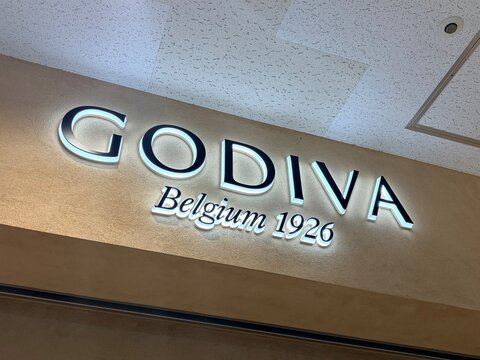 Godiva Belgium 1926 luxury chocolate shop illuminated storefront sign with glowing white letters mounted on a textured exterior wall in Chiyoda - Tokyo, Japan, December 25, 2025