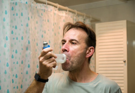 Man using asthma inhaler with spacer for respiratory relief