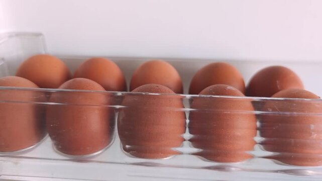 Brown eggs gradually shift in a clear plastic carton, showcasing a continuous arrangement of eggs in a neat row against a plain white background