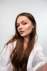 Fototapeta premium Young woman with long brown hair posing confidently against a white background, wearing a white shirt