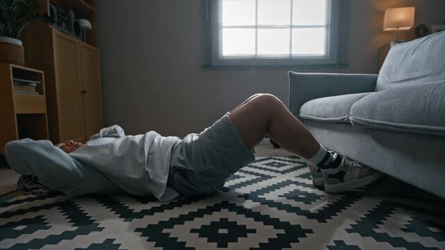 Side view shot of Biracial woman with braided hair doing crunches on floor in her apartment while exercising at home during her arrest