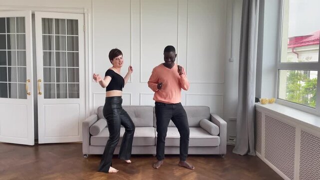 Couple of young african american man and caucasian woman dancing at home