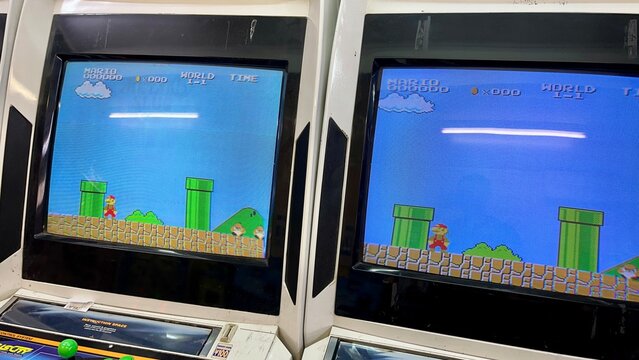 Retro arcade cabinets running Super Mario Bros game showing World 1-1 with classic green pipes and character sprite in a Japanese game center - Osaka, Japan, December 14, 2023