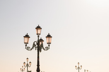 Obraz premium Ornate Lamppost With Distant Lights and Open Sky. A decorative Venice lamppost is isolated against a soft bright sky.