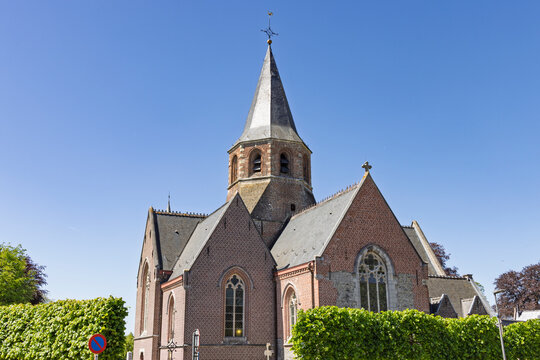Schelderode, Belgium. A beautiful brick parish church featuring a unique octagonal spire and gothic windows, set against a vibrant blue sky in the Belgian countryside.