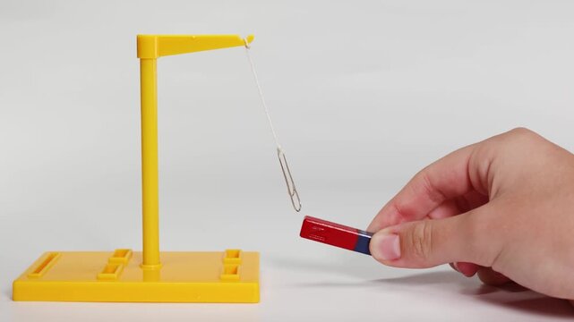 A close up shot of a person moving a magnet causing a paperclip to swing back and forth, demonstrating magnetic force.