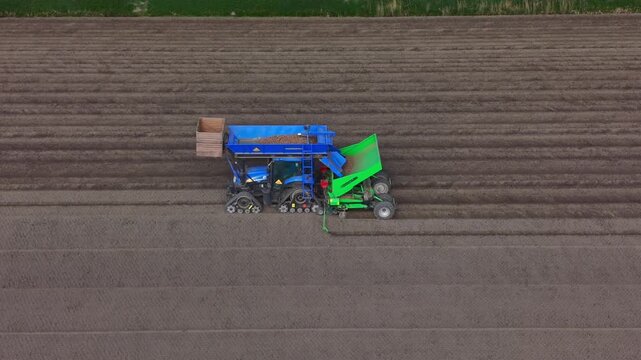 Aerial view of a blue tractor with a green attachment planting seeds in a brown agricultural field with parallel furrows Middenbeemster, North Holland, Netherlands.