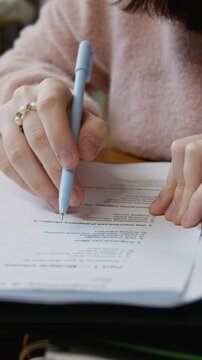 Vertical close-up of hands of anonymous teenage student girl in pink jumper completing exam test on pregnancy and reproductive health, marking correct answers in circle to achieve good grades
