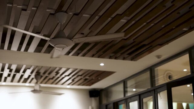 Low angle view of white ceiling fan spinning against modern wooden slatted interior design.