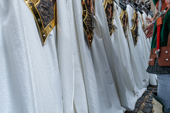 Detalle de fila de capas blancas bordadas y escudos met&aacute;licos en un desfile, Alcoy, Espa&ntilde;a