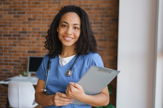 Portrait of young african-american female nurse at home, professional healthcare worker indoors, caregiver in home care setting, medical support and friendly assistance concept copy space