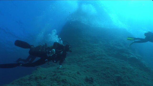  scuba divers exploring   reefs walls and caverns  underwater deep blue water big rocks and bubbles ocean scenery 