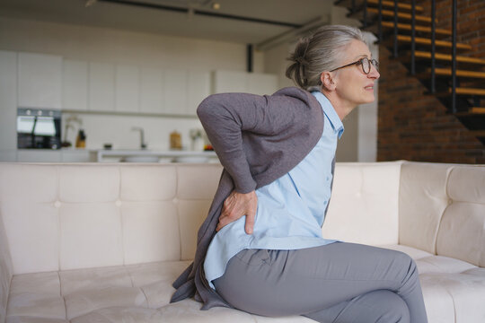 Senior woman suffering from back pain at home, elderly health problem, lower back discomfort, healthcare concept, pain relief, wellness and medical support need