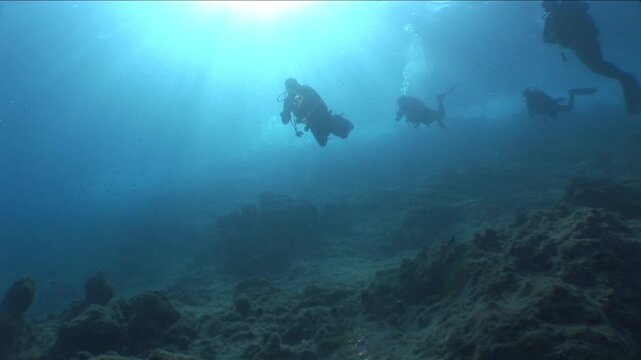  scuba divers exploring   reefs walls and caverns  underwater deep blue water big rocks and bubbles ocean scenery 
