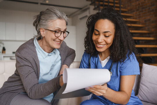 Close up of senior woman signing documents with nurse at home, healthcare paperwork, patient consent, medical forms, caregiver assistance, elderly care and home care service concept