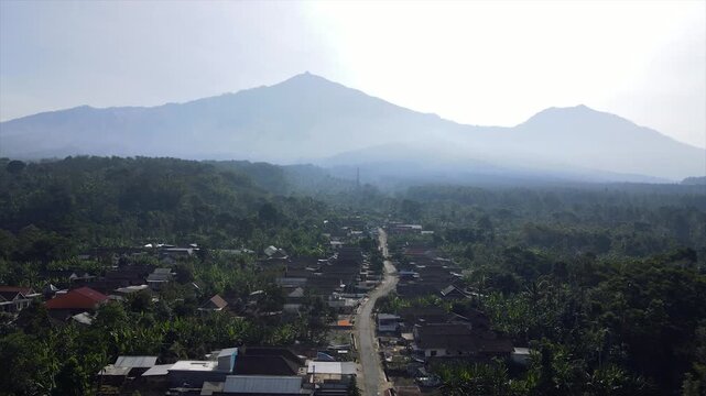 4K aerial drone footage of a peaceful rural village at the foot of the misty peaks of Mount Arjuna.