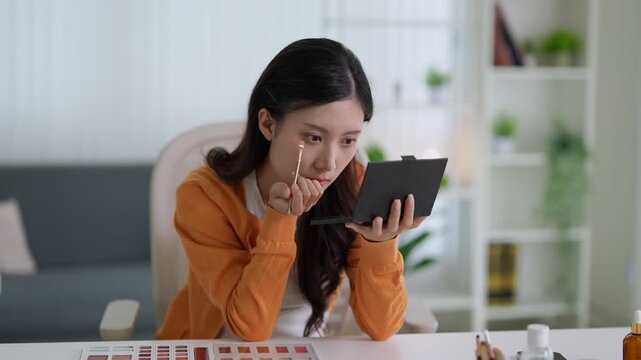 young Asian women applying makeup looking mirror at home beauty routine cosmetics products skincare tutorial online shopping ecommerce lifestyle bright modern