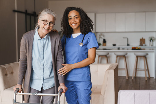 Senior woman standing with walker and young female nurse at home, both looking at camera, elderly patient with caregiver, mobility support, healthcare service and home care concept