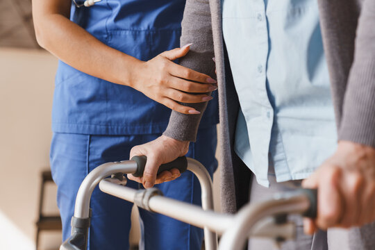 Close up of senior woman walking with walker while nurse helps her at home, caregiver supporting elderly patient with mobility assistance, rehabilitation, home care service and healthcare concept