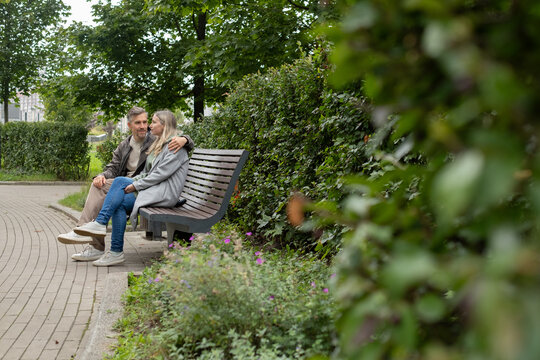 Couple sitting hugging on bench in green park. Romantic moment