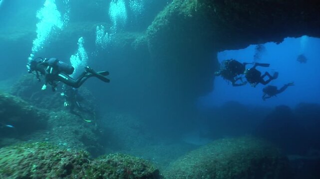 scuba divers exploring and swimming around an arc underwater cave and tunnel swim trough 