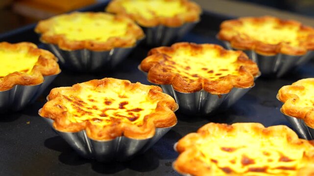 Rows of fresh homemade Taiwanese egg tarts resting on a black baking tray in a small bakery