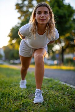 Woman stretching hamstrings in white athletic wear outdoors enjoying music
