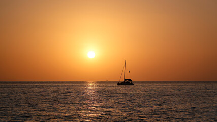 Sailboats drift gently on the tranquil sea, embraced by the breathtaking colors of a orange sunset © aapsky