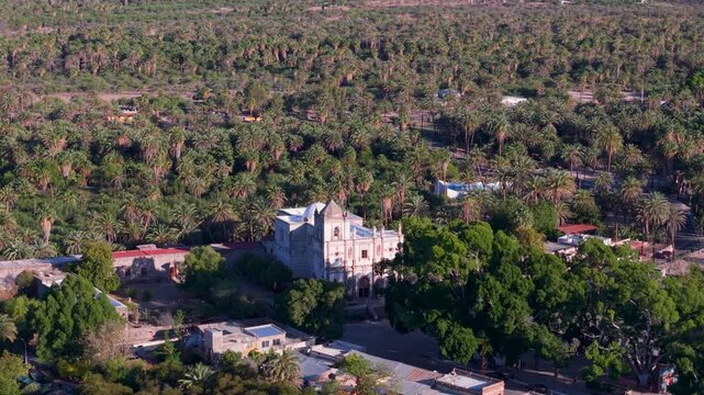 See aerial perspectives of Mission Church in San Ignacio, showcasing the surrounding oasis landscape and nearby buildings.
