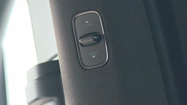 Control switch for vehicle window operation showing open and close positions, mounted on a door panel with a sleek design and modern aesthetic in a vehicle interior