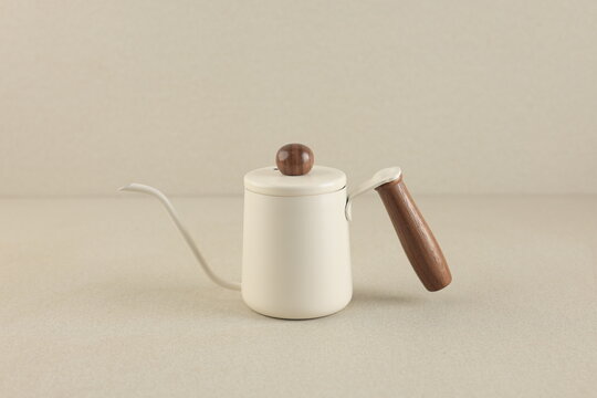 a white kattle with a wooden handle, and a slight wooden accent on the top. isolated on a clean natural beige background, with bright light