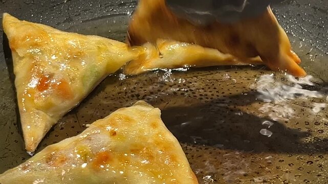 Tongs removing crispy golden samosas from hot frying oil
