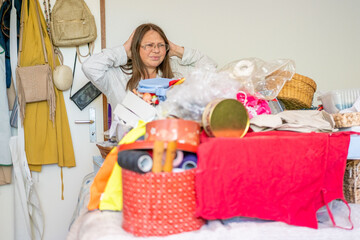 Stressed Middle aged woman with glasses raises hands in frustration standing before pile cluttered items, Home organization sorting household items, Cleaning routine clutter lifestyle transformation © kittyfly
