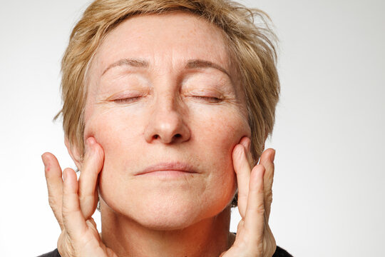 Portrait of senior woman touching face with natural skin texture and calm expression.