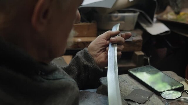 Elderly craftsman working in his old workshop, carefully restoring collectible Japanese bladed weapons