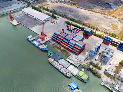 Aerial view of barges loading cargo and a container yard at a riverside terminal in Ho Chi Minh City, Vietnam