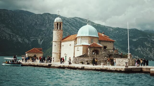 Cinematic aerial drone footage of Our Lady of the Rocks near Perast. Historic island church surrounded by the turquoise waters of the Bay of Kotor with dramatic mountain scenery