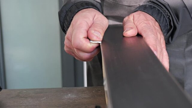 Handheld close up video shows hands manually sharpening ski edge with metal tool while ski is fixed in workshop vise during detailed winter sports maintenance 2026