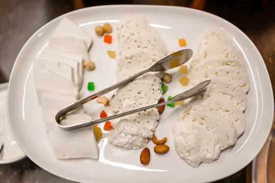 Fresh cheese platter with soft goat cheese slices, nuts and tongs on a white plate for appetizer