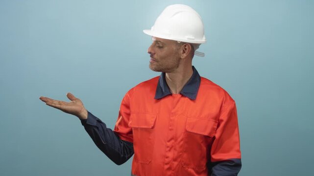 Man builder wearing white hardhat and orange coverall shows open palm up in studio; quiet contemplation mood.
