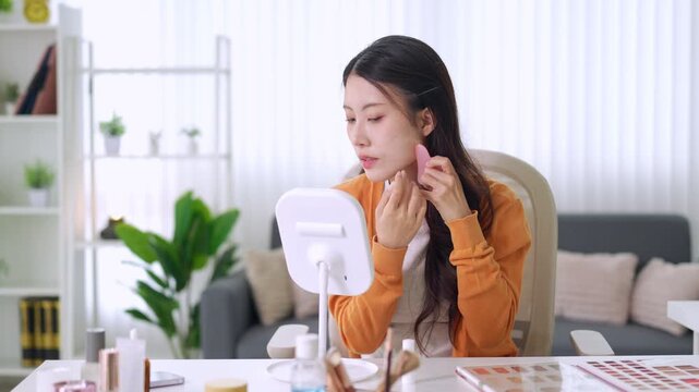young Asian women beauty blogger recording makeup tutorial video content creator vlogger applying cosmetics using ring light mirror filming at home office