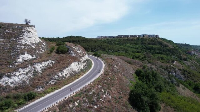 Aerial view of a winding asphalt road curving through white cliffs and lush green hills overlooking the Black Sea coast, Balchik, Dobrich Province, Bulgaria.