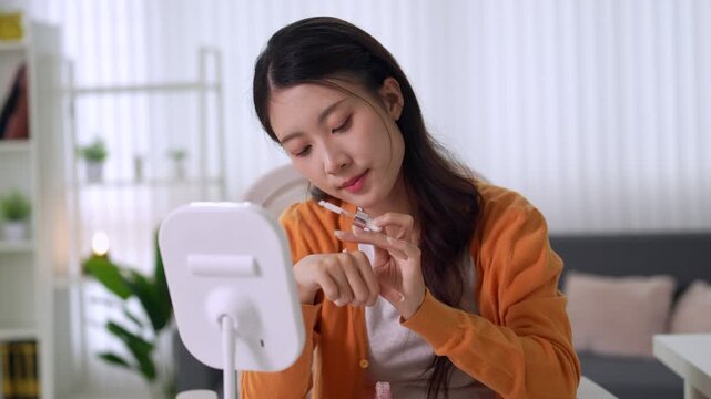 young Asian women applying makeup brush cosmetics beauty routine filming video tutorial content creator recording vlog with ring light modern home living room