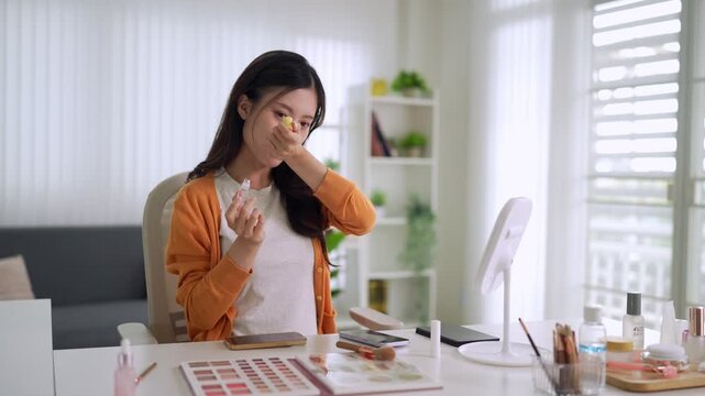 Asian beauty blogger influencer testing makeup cosmetics reviewing product live streaming tutorial video call sitting desk home office bright natural light