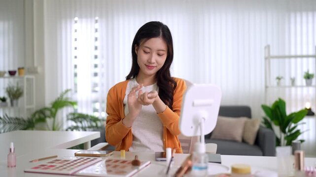 young Asian women beauty influencer testing skincare cosmetics product creating makeup tutorial video content recording review at bright modern home studio