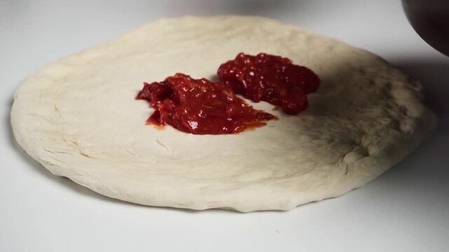 Spreading tomato sauce on a raw pizza dough base with a spoon