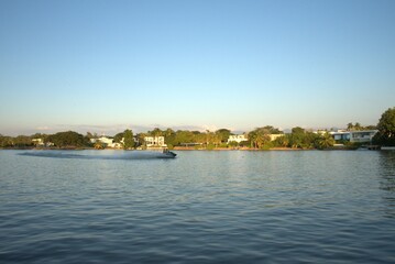 Naklejka premium Personal watercraft speeding across a calm lake with luxury waterfront houses and tropical trees