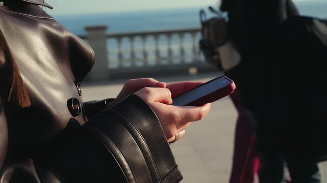 A close-up of hands holding a smartphone while walking outside. The woman actively uses the device during her walks: browsing social media, reading news, and sending messages. The focus is on modern